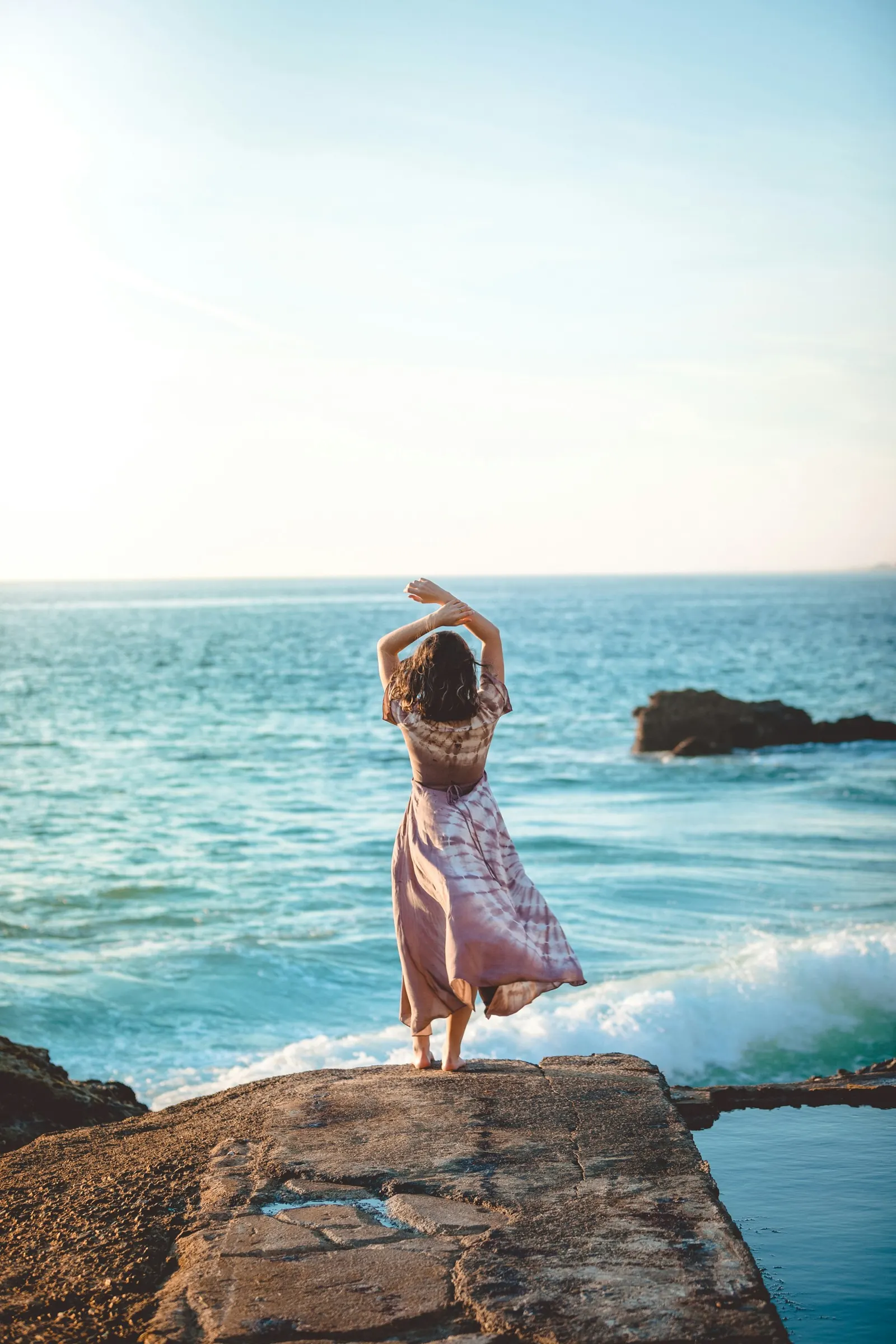 A woman standing on rocks by the sea with her arms raised, feeling free